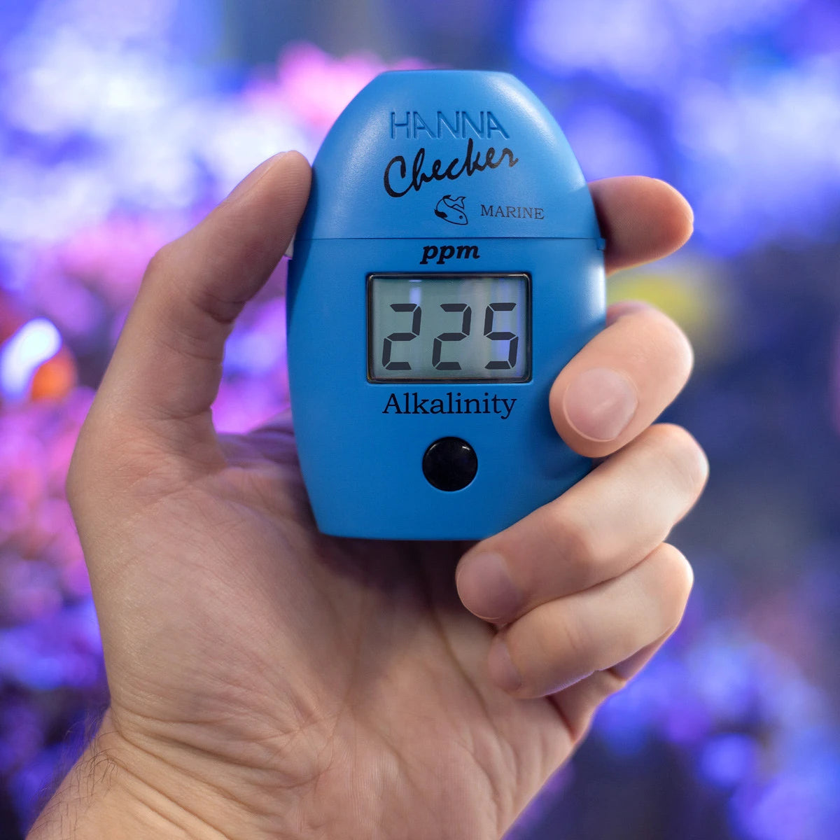 Hanna Checker HC HI755 marine alkalinity held in hand in front of a reef aquarium